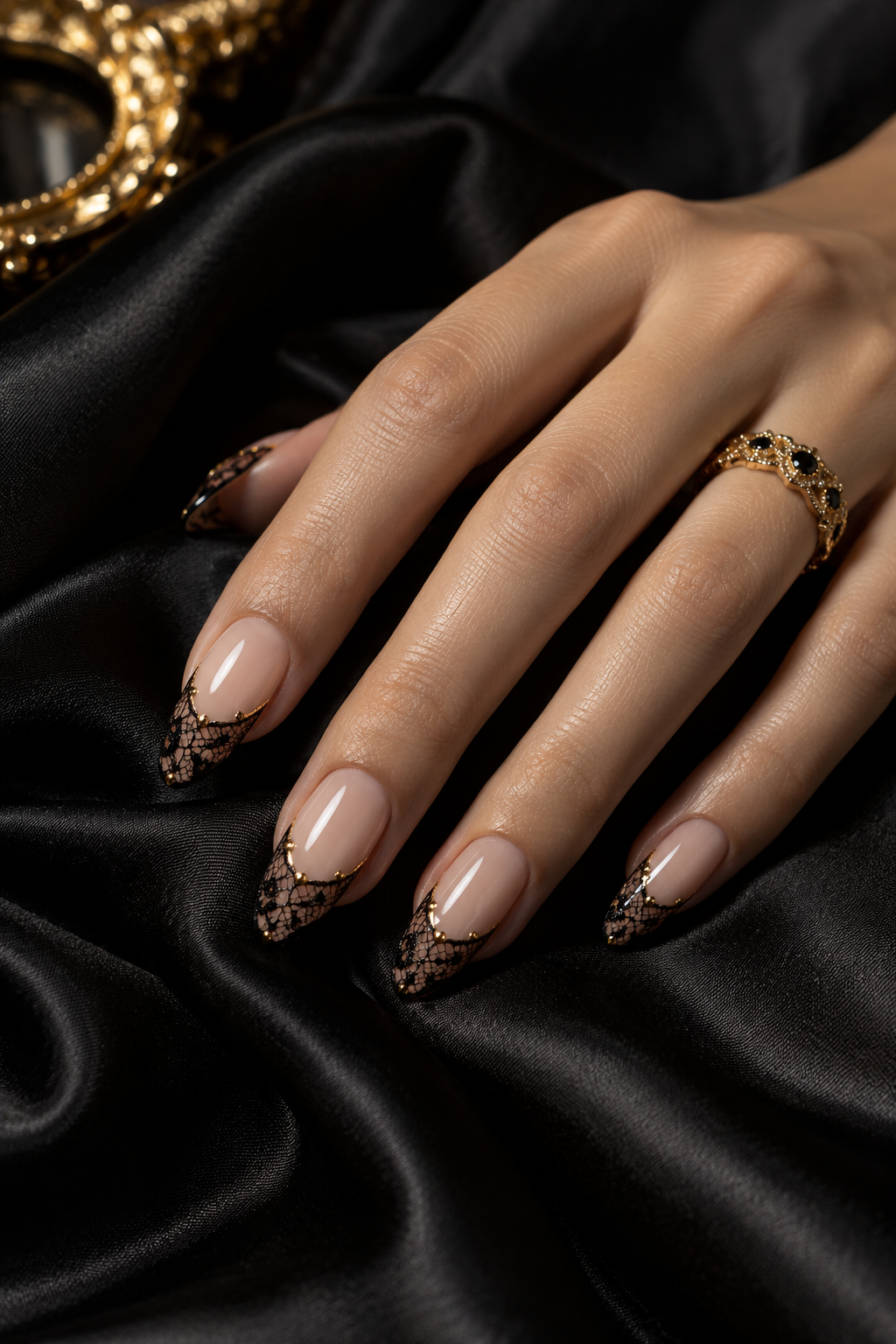 Nude almond nails with intricate black lace tips and gold accents